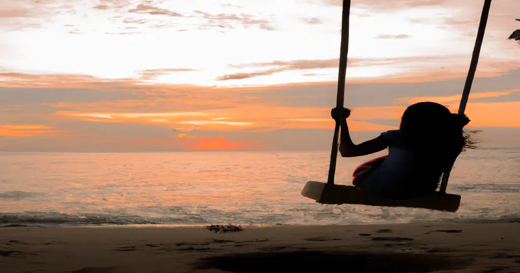 Beach swing during sunset with silhoutte of girl swining on it