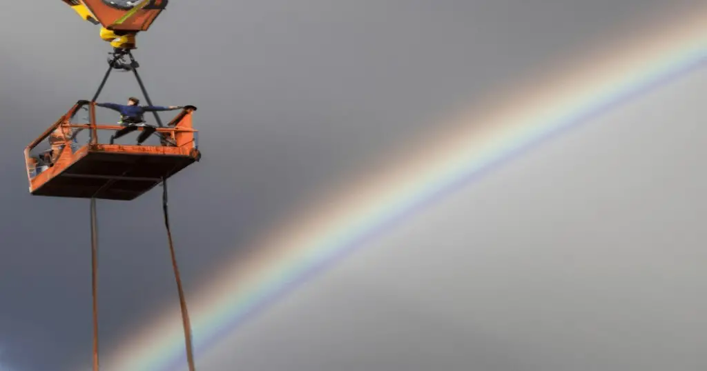 Bungee jumper on a crane in gravity park with rainbow in the background