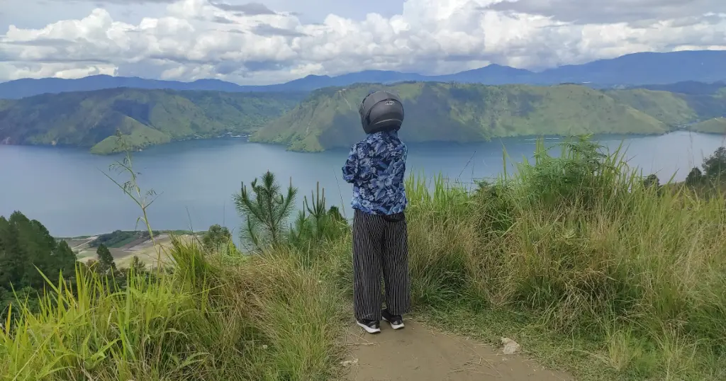 A girl wearing a motorbike helmet standing on a viewpoint on Samosir overlooking Lake Toba