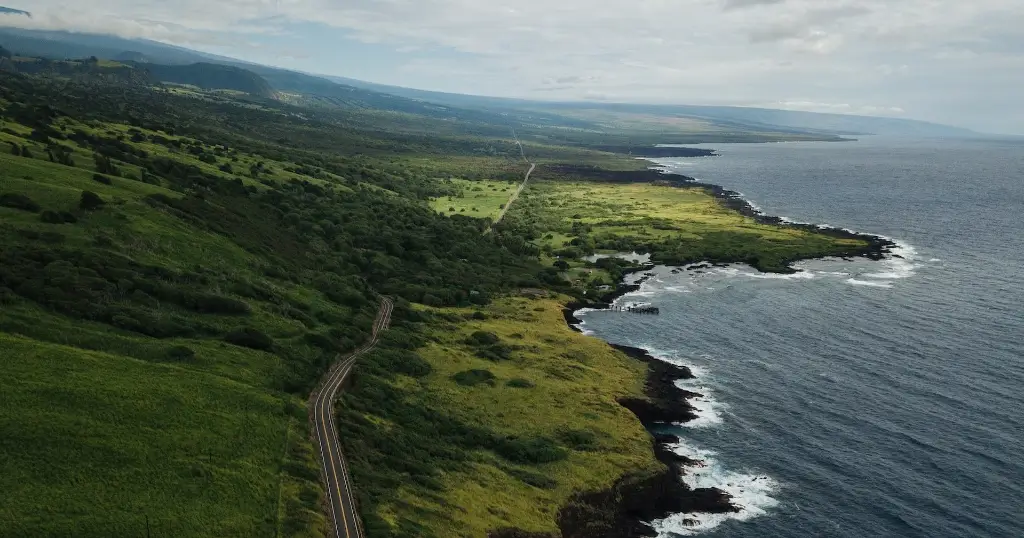 Drone shot of a lonely coastal road running a long a lush-green shore on the Big Island of Hawaii