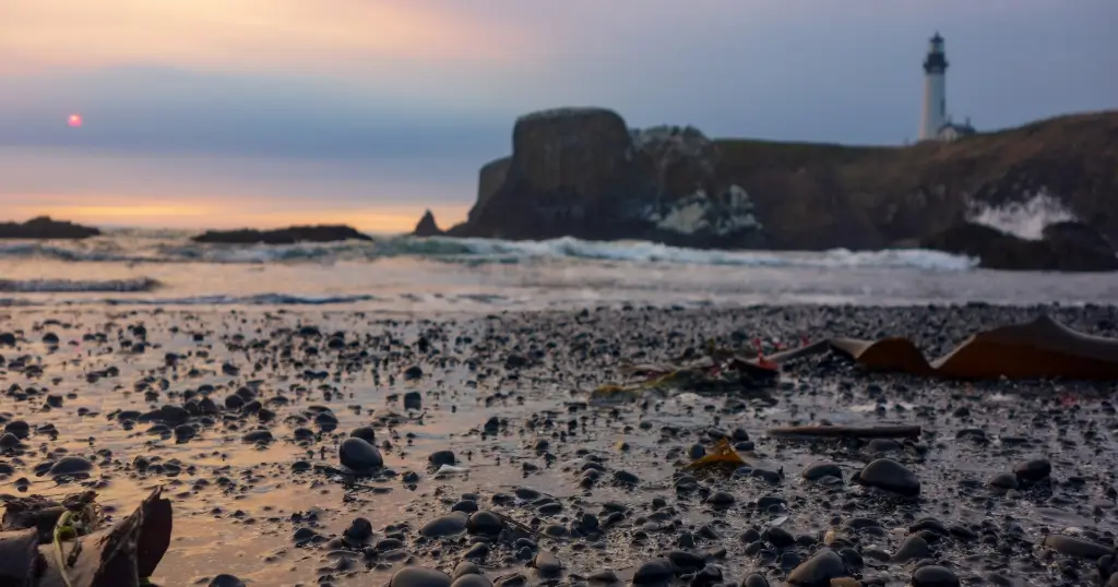 The beach in front of Yaquina Head Lighthouse during low-tide with the sun setting in the background