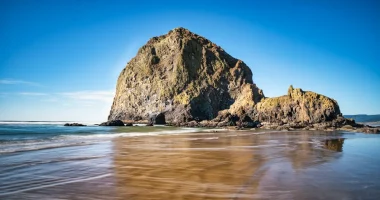 Unique, steep rock formation at Cannon Beach in Oregon with wet sand reflecting the rocks.